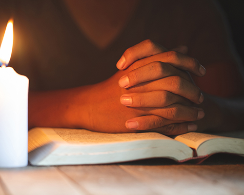stock photo of praying person with Bible in candlelight